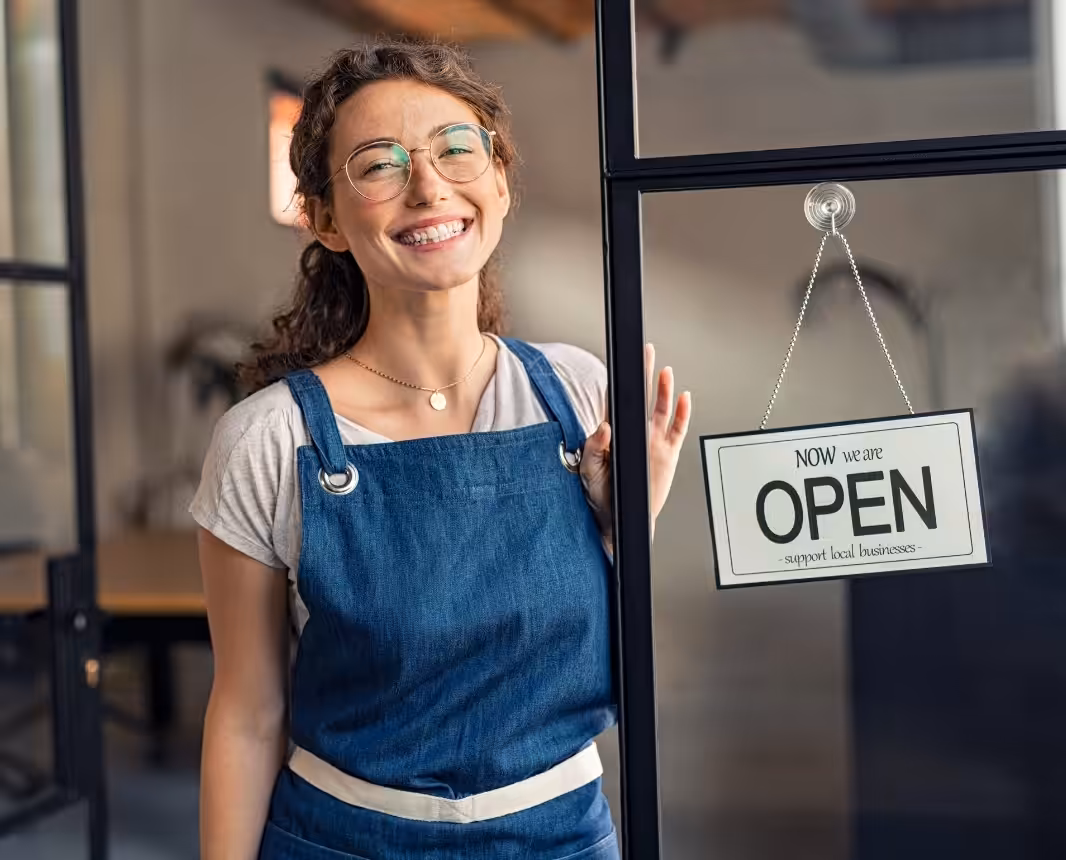 Small business owner standing by an Open sign at a storefront